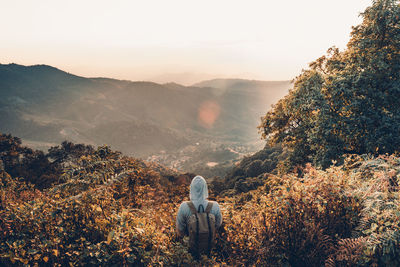 Rear view of woman sitting on mountain against sky