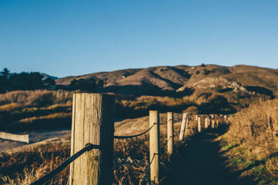 Close-up of fence on landscape against clear blue sky