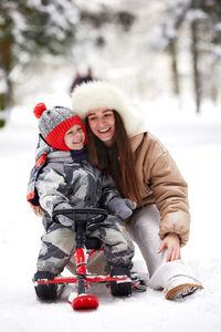 Portrait of smiling woman sitting on snow covered field