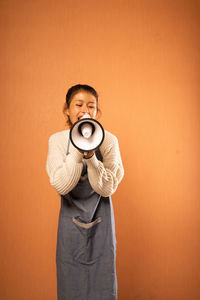 Portrait of young woman standing against yellow background