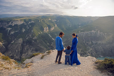 Family of three people stands on the mountain gorge during sunset in dagestan