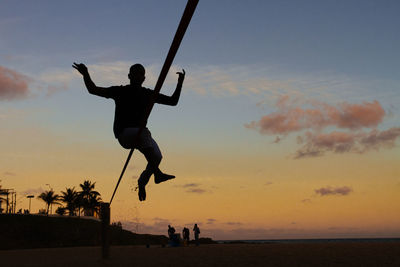 Full length of silhouette man jumping at beach against sky during sunset