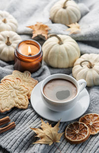 White pumpkins, coffee and autumn leaves on a grey knitted sweater. autumn home decor.