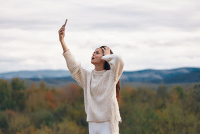 Young woman with arms raised standing against sky