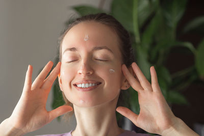 Smiling young woman taking some moisturizing face cream or lotion and applying. facial skin care.