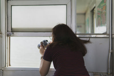 Rear view of woman photographing through window at home