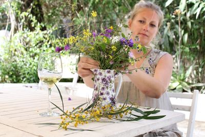 Woman putting flowers in vase at back yard