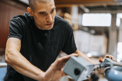 Focused male worker installing machine part while working in manufacturing factory