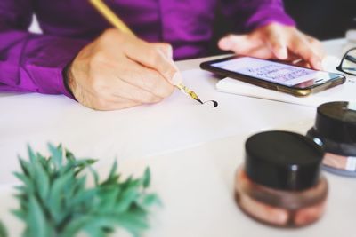 Calligraphy expert writing with fountain pen while using mobile phone