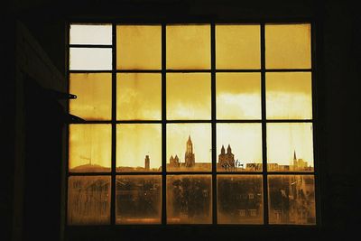 Silhouette building against sky seen through glass window