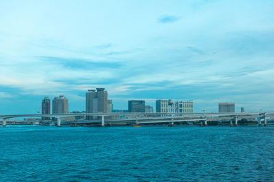 Sea by modern buildings against sky in city