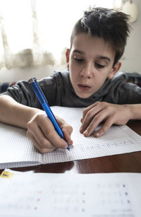 Boy writing in book while sitting on table