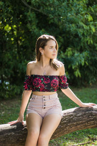 Thoughtful teenage girl looking away while sitting against trees in park