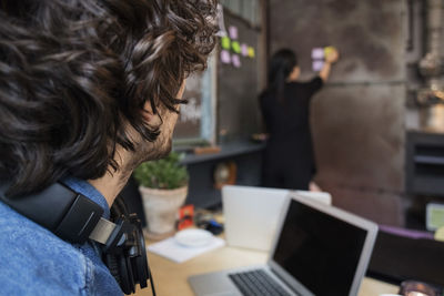 Midsection of creative businessman looking at female coworker sticking adhesive note on wall