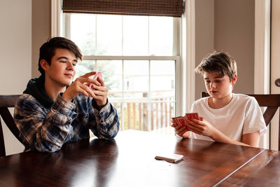 Two teenage boys playing cards at the kitchen table together.