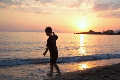 Side view of silhouette boy walking at beach against sky during sunset