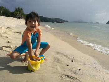 Portrait of cute boy playing with sand at beach against sky