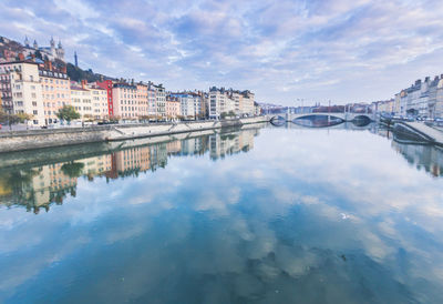 Bridge over river amidst buildings in city against sky