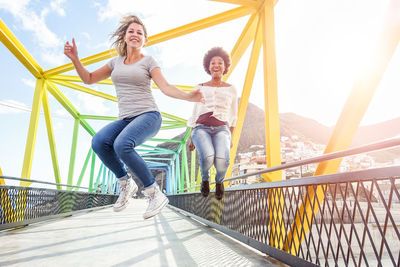 Portrait of happy friends jumping over bridge in city