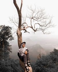 Man standing by bare tree on mountain against sky