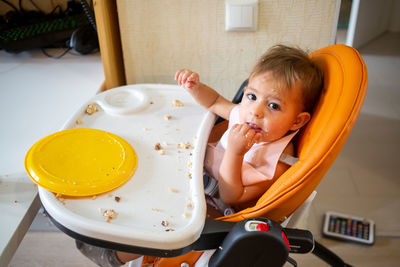 High angle view of cute baby girl sitting on wheelchair at home