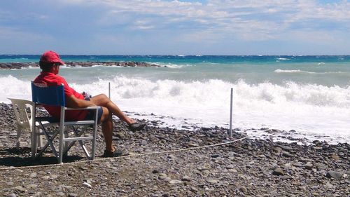 Man sitting on chair at beach against sky