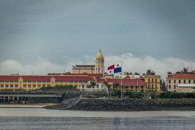 Buildings by sea against cloudy sky