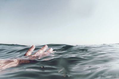 Cropped hand swimming in sea against clear sky