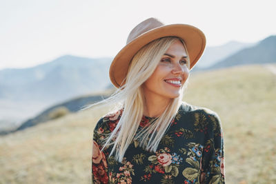 Close-up of smiling young woman wearing hat looking away while standing on field