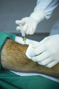 Cropped hand of surgeon injecting syringe in patient leg at hospital