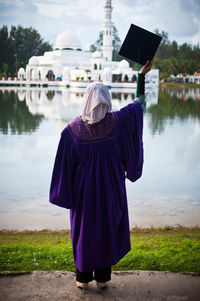 Rear view of woman with umbrella standing by lake