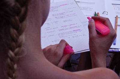 Cropped image of woman holding pink highlighter with documents at table