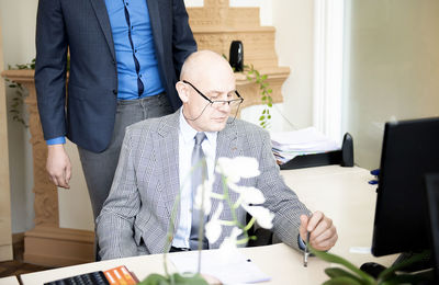  mature businessman in classic suit is using a computer and a pen while working in his office