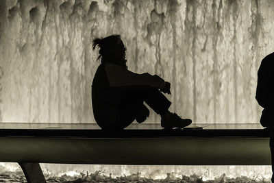Low section of silhouette people sitting by water