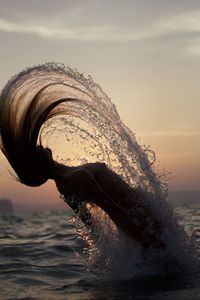 Sea waves splashing on shore against sky during sunset