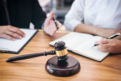 Midsection of lawyers with books and pens sitting by gavel on desk