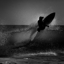 Silhouette man surfboarding through waves against sky