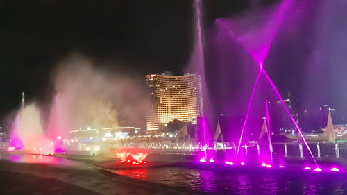 Illuminated city by river against sky at night