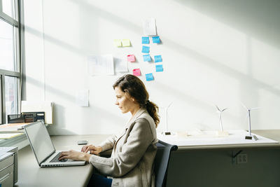 Side view of businesswoman using laptop while working by wind turbine models arranged on desk