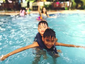 Portrait of smiling boy piggybacking brother in swimming pool