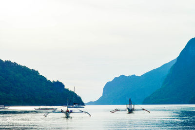 Outrigger boats in sea against clear sky