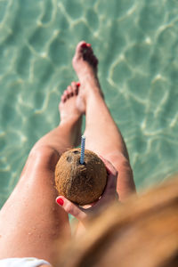 From above of unrecognizable female sitting with coconut cocktail with straw near blue rippling sea and enjoying summer holiday on playa de muro