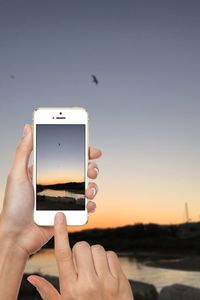 Close-up of hand holding mobile phone at beach against clear sky