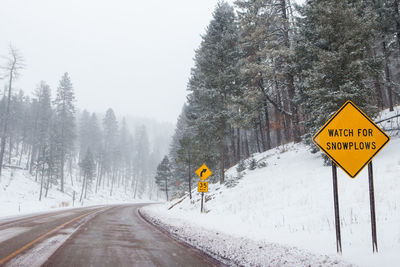 Road sign by snow covered trees during winter