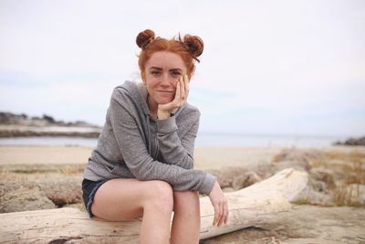 Portrait of smiling young woman sitting on beach against sky