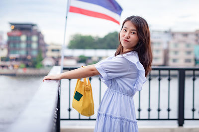 Portrait of young woman standing by railing in city