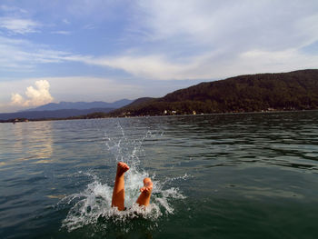 Low section of person diving in lake against sky