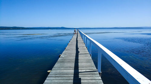 Wooden pier on sea against clear blue sky