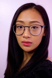 Close-up portrait of young woman wearing eyeglasses against wall