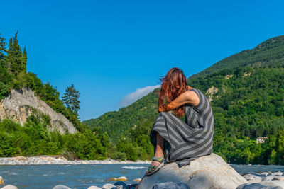 Woman sitting on mountain against sky